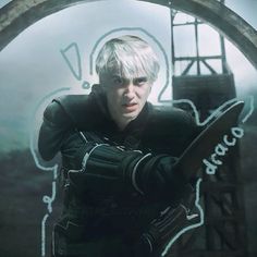 a man with white hair holding a knife in front of a circular window that has graffiti on it