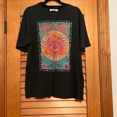 a black t - shirt with an eye on it hanging from a wooden closet door