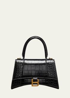 "Find BALENCIAGA Hourglass Small Top-handle Bag on Editorialist. The Balenciaga Hourglass Small Top-Handle Bag is crafted from crocodile-embossed calfskin leather. It features a rolled top handle, a removable and adjustable crossbody strap, and a flap top with a hanging \"B\" hardware and a snap closure. The bag also has an exterior slip compartment at the back and an interior slip pocket. The dimensions of the bag are 5.5\"H x 9.1\"W x 3.9\"D. It is made in Italy." Balenciaga Hourglass Bag, Balenciaga Top Handle Bag, Balenciaga Top, Balenciaga Bag, Handle Bag, Small Tops, Crossbody Strap, Snap Closure, Calf Leather