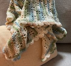 a crocheted blanket sitting on top of a couch next to a brown pillow