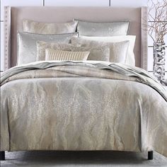 a bed with gold and silver comforters in a white room next to a window