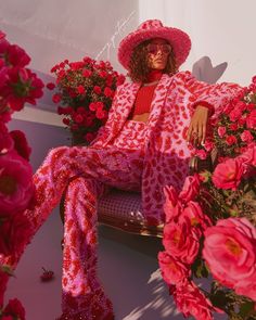 a woman sitting on top of a bench next to flowers and wearing a pink hat