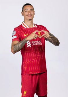 a man in a liverpool united kit making a heart sign with his hands while standing against a white background