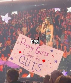 a woman holding a sign that reads real pretty girls listen to guts on the stage