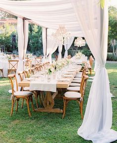 an outdoor dining table with white drapes and chandelier hanging from the ceiling