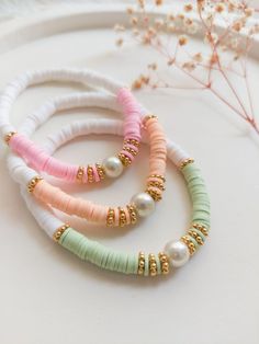 three different colored bracelets with pearls and beads on top of a white table next to a plant