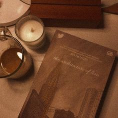 an old book is sitting on a table next to two candles and a glass cup