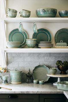 the shelves are filled with green dishes and plates on top of each other in front of a white brick wall