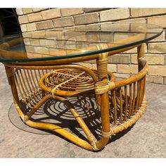 a rattan table with glass top and wicker base on concrete ground next to brick wall