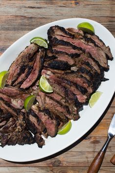 steak with lime wedges on a white plate next to a fork and utensils