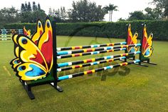 a set of colorfully painted fences in the middle of a grass field with trees and bushes behind it