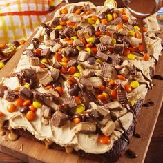 a cake with chocolate, candy and candy corn on it sitting on a wooden cutting board