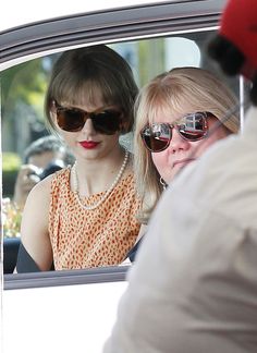 two women are sitting in the back seat of a car and one is wearing sunglasses