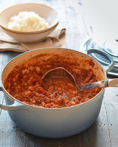 a large pot filled with food on top of a wooden table next to a bowl of mashed potatoes