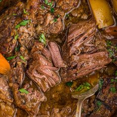 a pot filled with meat and carrots on top of a wooden table next to a spoon