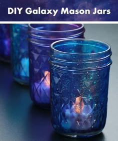 some glass jars with blue and purple designs in them on a tabletop, next to the caption diy galaxy mason jars