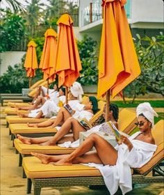 several women are lounging on lounge chairs under umbrellas and reading the book in front of them