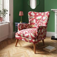 a red chair sitting in front of a green wall next to a fire place with a lamp on top of it