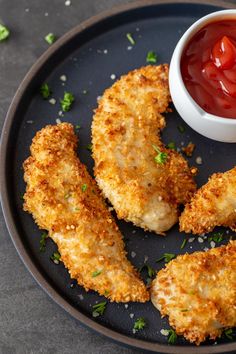 fried chicken with ketchup and parsley on a black plate next to a small white bowl