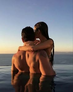 two people sitting on the back of a swimming pool with their arms around each other