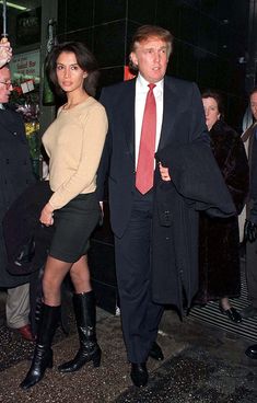 a man and woman dressed in business attire walking down the street with an umbrella over their heads