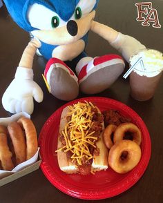 a stuffed animal sitting next to a plate with donuts and hotdogs on it