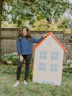 a woman standing next to a cardboard house