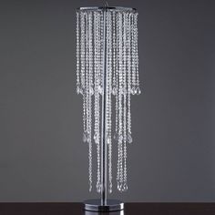 a tall crystal beaded lamp on a table with a black base and grey wall in the background