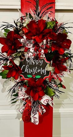 a christmas wreath hanging on the side of a door with red flowers and greenery