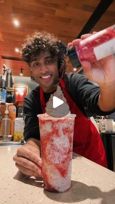 a man is pouring something into a drink in a red and white cup while sitting at a counter