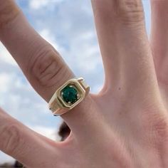 a person's hand with a ring on it and an emerald stone in the middle