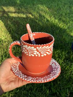 a hand holding a cup with a spoon in it on top of a saucer