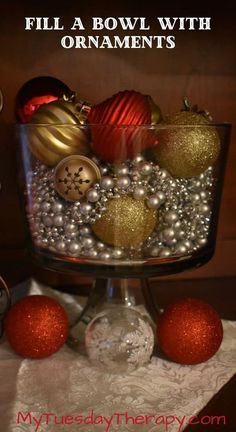 a glass bowl filled with ornaments on top of a white table cloth next to red and gold balls