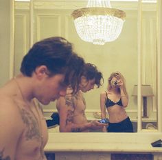 three people are looking at their cell phones in front of a mirror with a chandelier