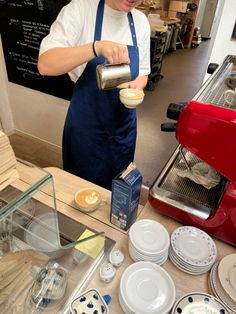 a woman pouring something into a cup on top of a counter next to plates and cups