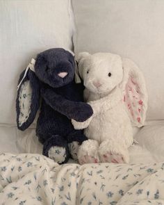 two stuffed animals sitting next to each other on a bed