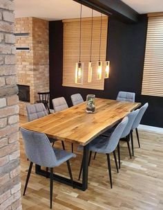 a wooden table surrounded by grey chairs in front of a brick wall and window with blinds