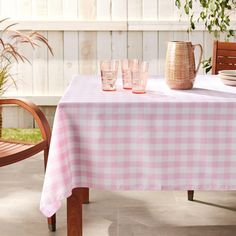 the table is set with pink gingham cloths and glasses on it, next to a potted plant