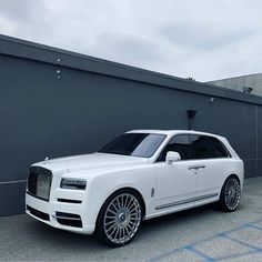 a white rolls royce parked in front of a gray wall with chrome wheels and rims