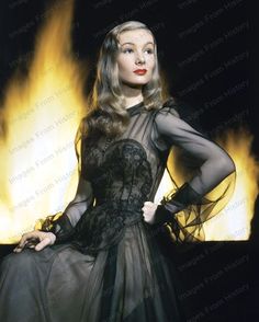 a woman in a black dress standing next to a fire filled wall with her hands on her hips