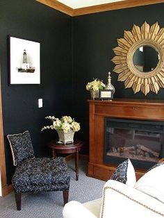 a living room with black walls and white furniture in front of a fire place that has a sun mirror on the wall