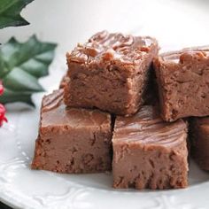 four pieces of chocolate fudge on a white plate with holly and red berries in the background