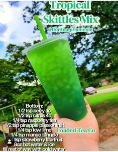 a person holding up a green drink in front of a sign that says tropical skittles mix