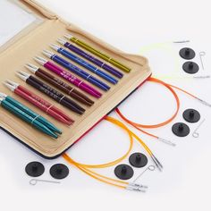 several different colored pens and markers in a zippered case on a white surface next to earbuds