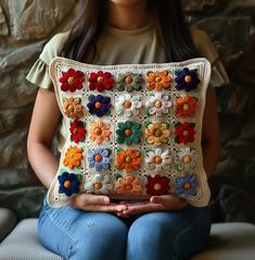 a woman sitting on a couch holding a crocheted pillow with flowers in it