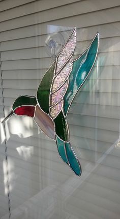 a stained glass hummingbird hanging on the side of a house