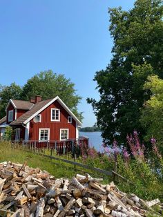 a red house sitting on top of a lush green hillside next to a lake with lots of trees