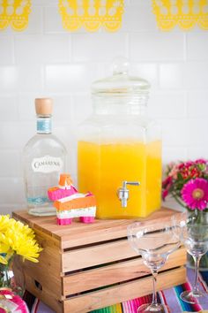 a table topped with drinks and flowers on top of a wooden crate next to a bottle