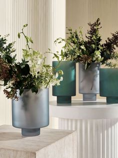 three vases filled with flowers sitting on top of a white table next to a mirror