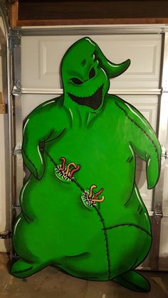 a large green cartoon character sitting in front of a garage door